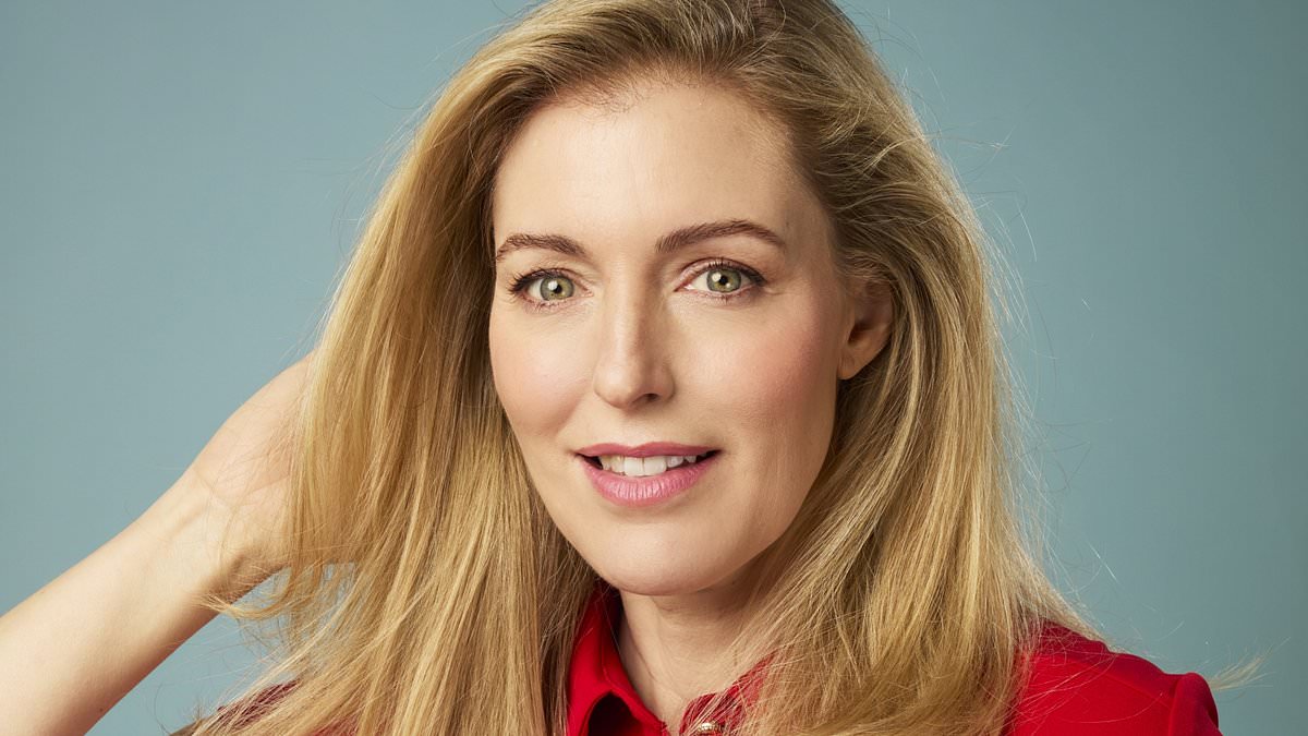 A woman with long blonde hair and a red shirt smiles at the camera, one hand in her hair, against a blue-grey backdrop.