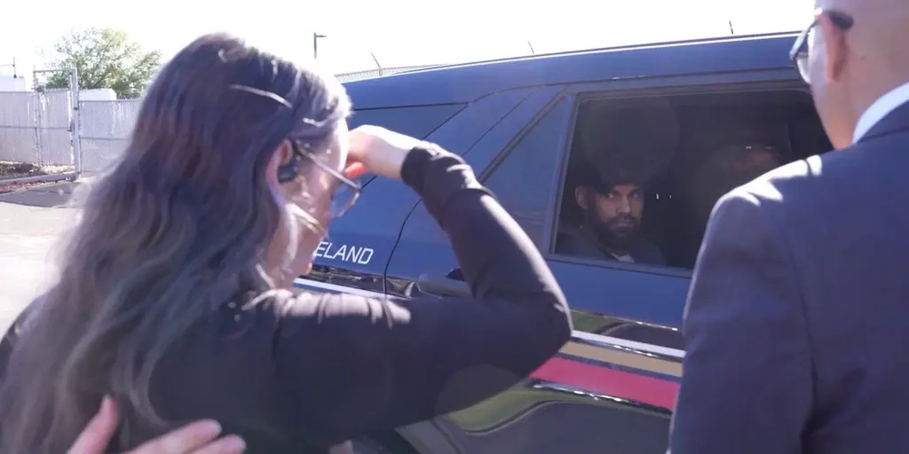 A woman raises a hand to her head beside an SUV as a bearded man looks out its window.